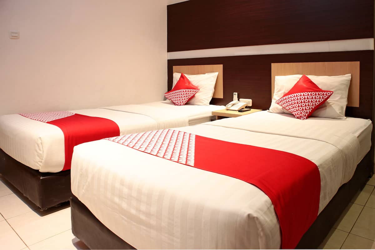 Two beds with white and red bedding, a wooden headboard, and a bedside table with a phone.