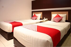 Two beds with white and red bedding, a wooden headboard, and a bedside table with a phone. - Hotel O Bumi Malaya (Medan)
