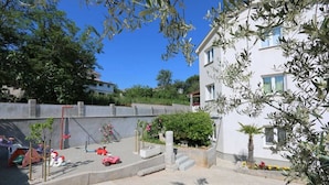 Zona residencial amb un edifici blanc, un parc infantil amb joguets i un cel serè.