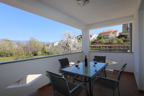 Un balcon avec une table en verre, des chaises et une bouteille de vin.