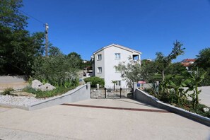 Un bâtiment à deux étages, doté d’une entrée fermée par un portail, entouré de verdure et surplombé d’un ciel dégagé.