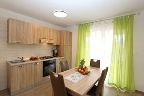 Une cuisine de taille réduite avec des meubles de rangement en bois, une table à manger avec des chaises et un panier de fruits.