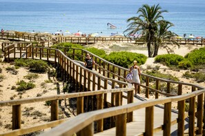 A wooden boardwalk leading to a beach with palm trees and umbrellas.