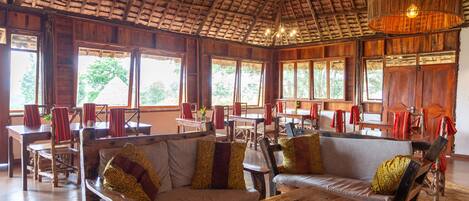 A spacious room with wooden furniture, large windows, and a thatched roof.