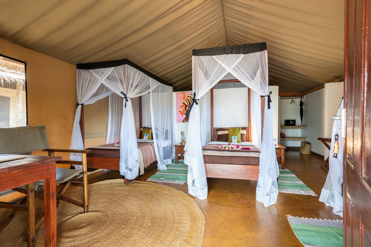 A room with two beds, each with a canopy, a wooden desk, and a woven mat on the floor.
