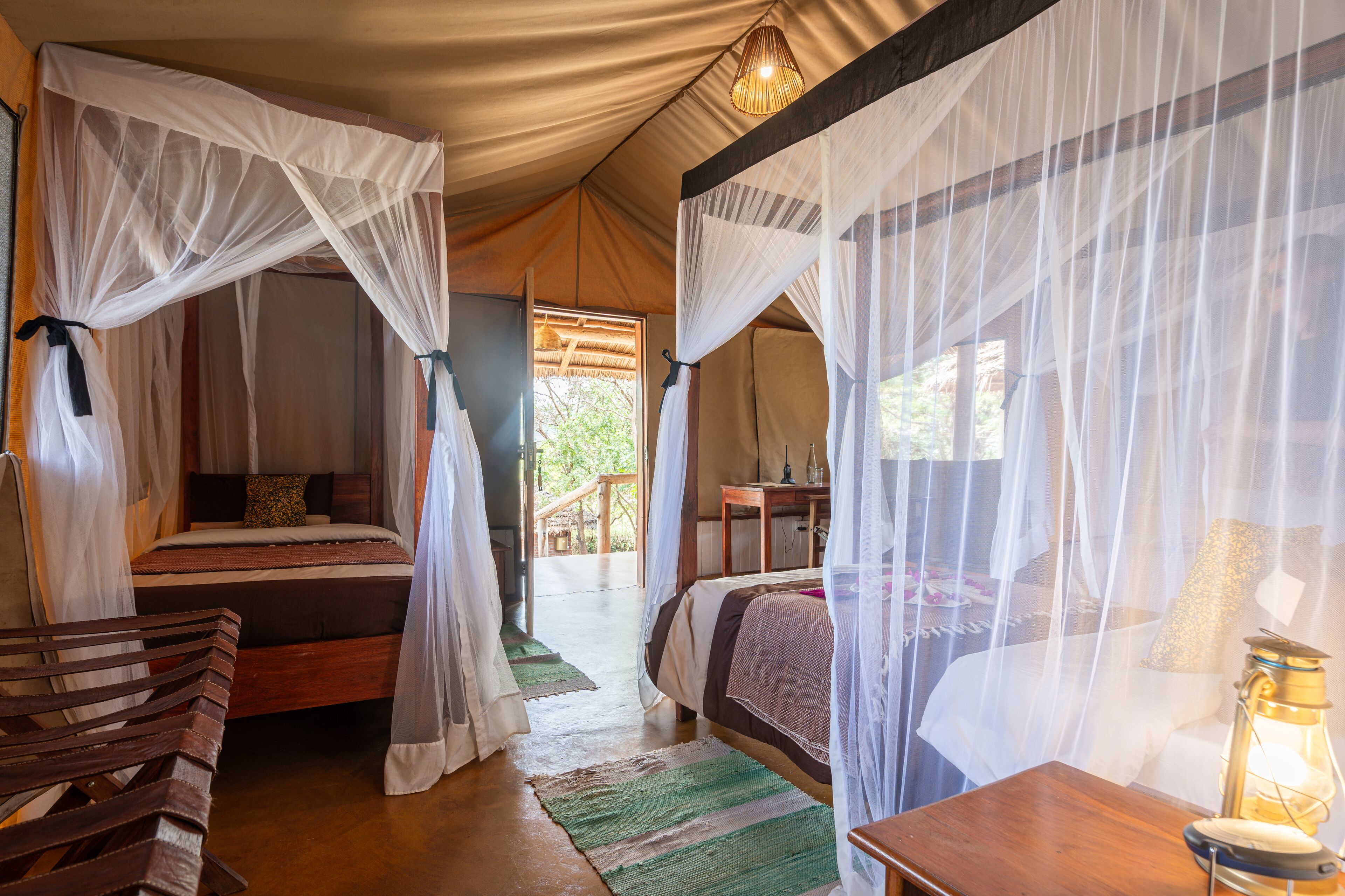 A tented accommodation with two beds, each with a canopy. There is a wooden bench and a table with a lantern.