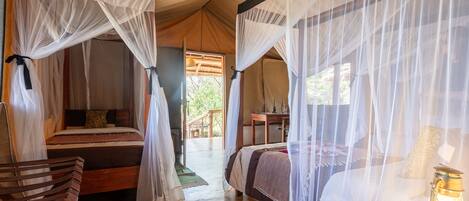 A tented accommodation with two beds, each with a canopy. There is a wooden bench and a table with a lantern.