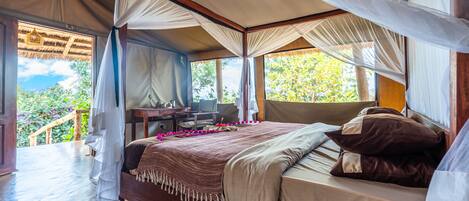 A bedroom with a canopy bed, a desk, and a view of the outdoors.