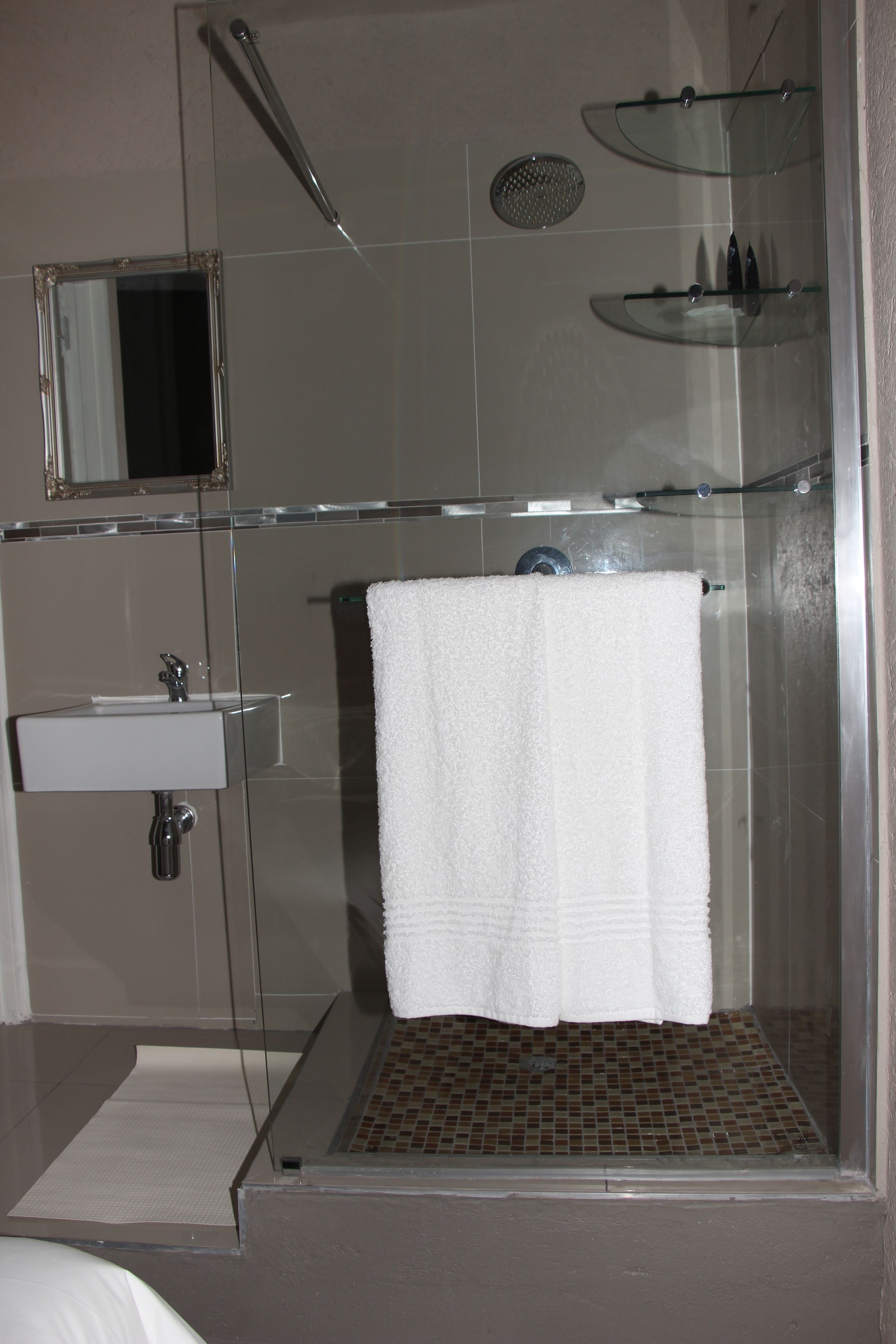Een moderne badkamer met een douchecabine van glas, een witte wastafel en een glazen plank met toiletartikelen.