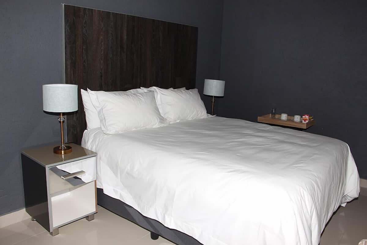 A neatly made bed with white linens, a dark headboard, and two bedside lamps.