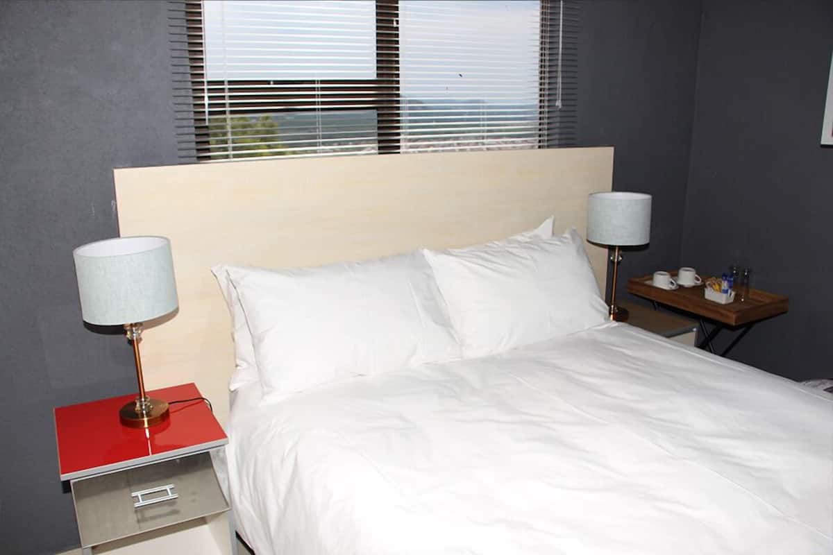 A hotel room with a bed, two bedside tables, a lamp on each table, and a window with blinds.