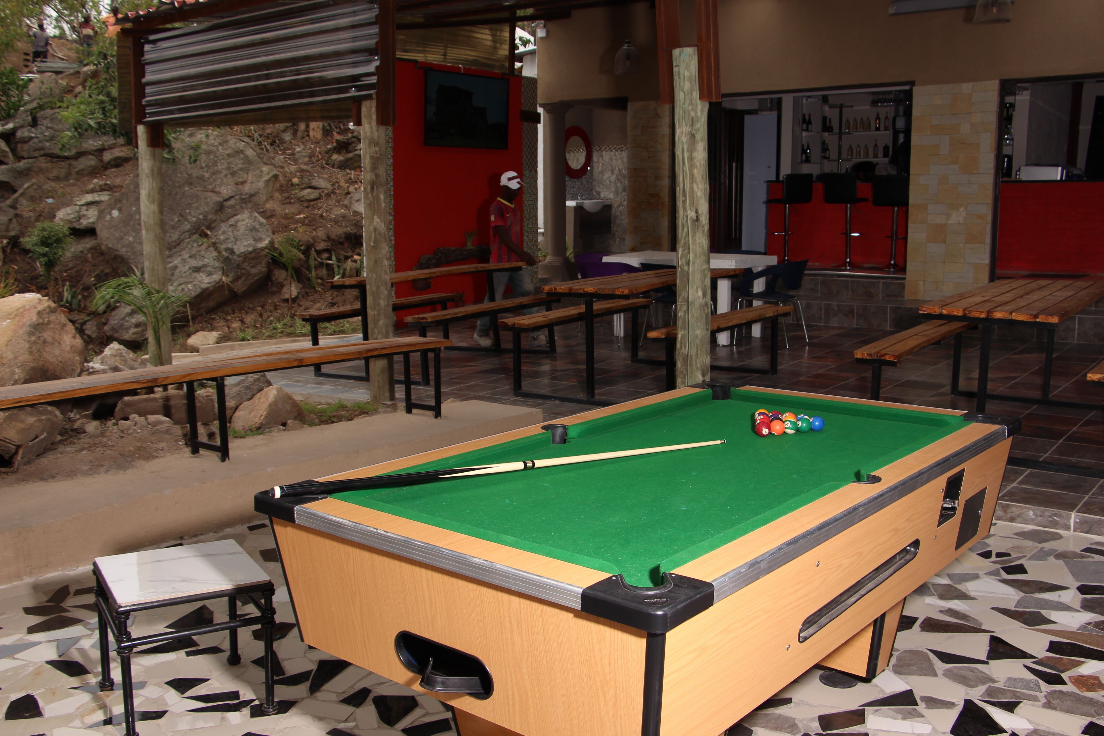 Una mesa de billar con bolas, bancos y una pared de piedra al fondo.