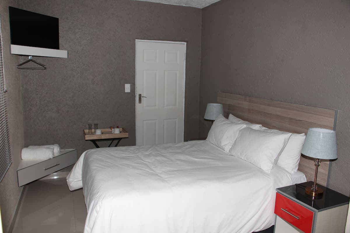 A neatly arranged hotel room with a bed, bedside table, lamp, and a small table with a mirror and a towel.