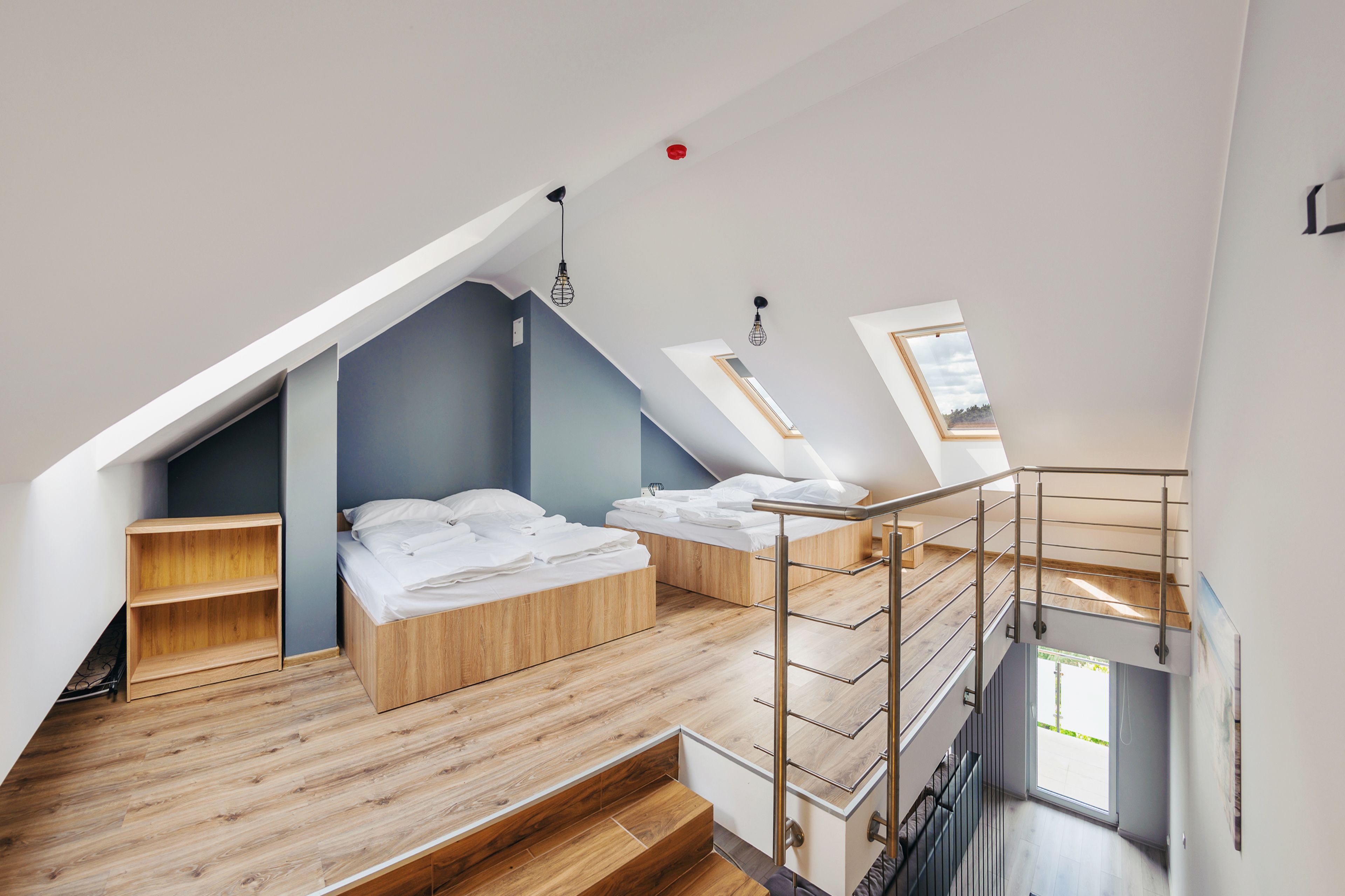 A modern loft bedroom with a sloped ceiling, built-in wooden shelving, a staircase, and a skylight.