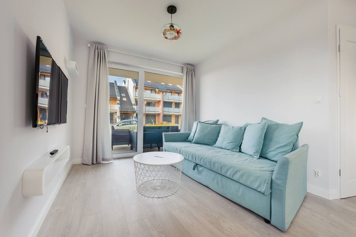A modern living room with a teal sofa, a round coffee table, and a TV mounted on the wall.
