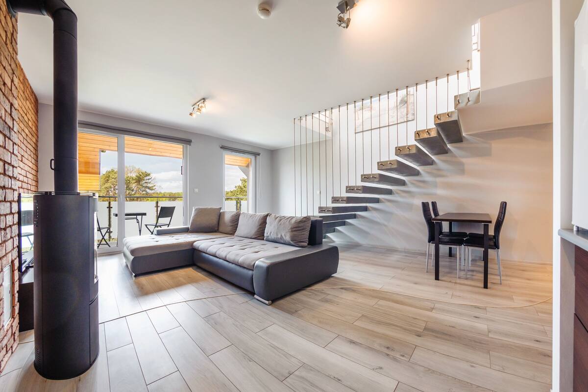 A modern living room with a sectional sofa, a dining area with a table and chairs, and a staircase with a unique design.