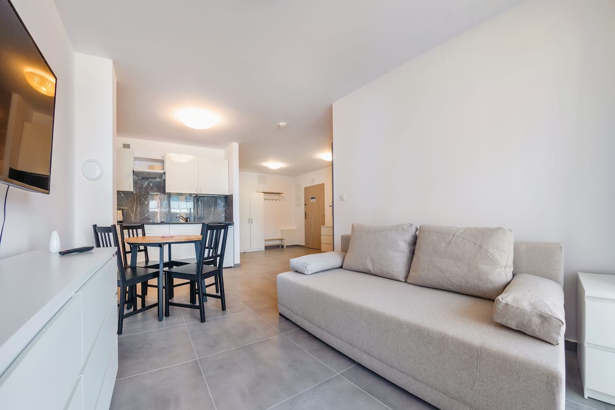 A modern living room with a sofa, a dining table with chairs, and a kitchen area in the background.