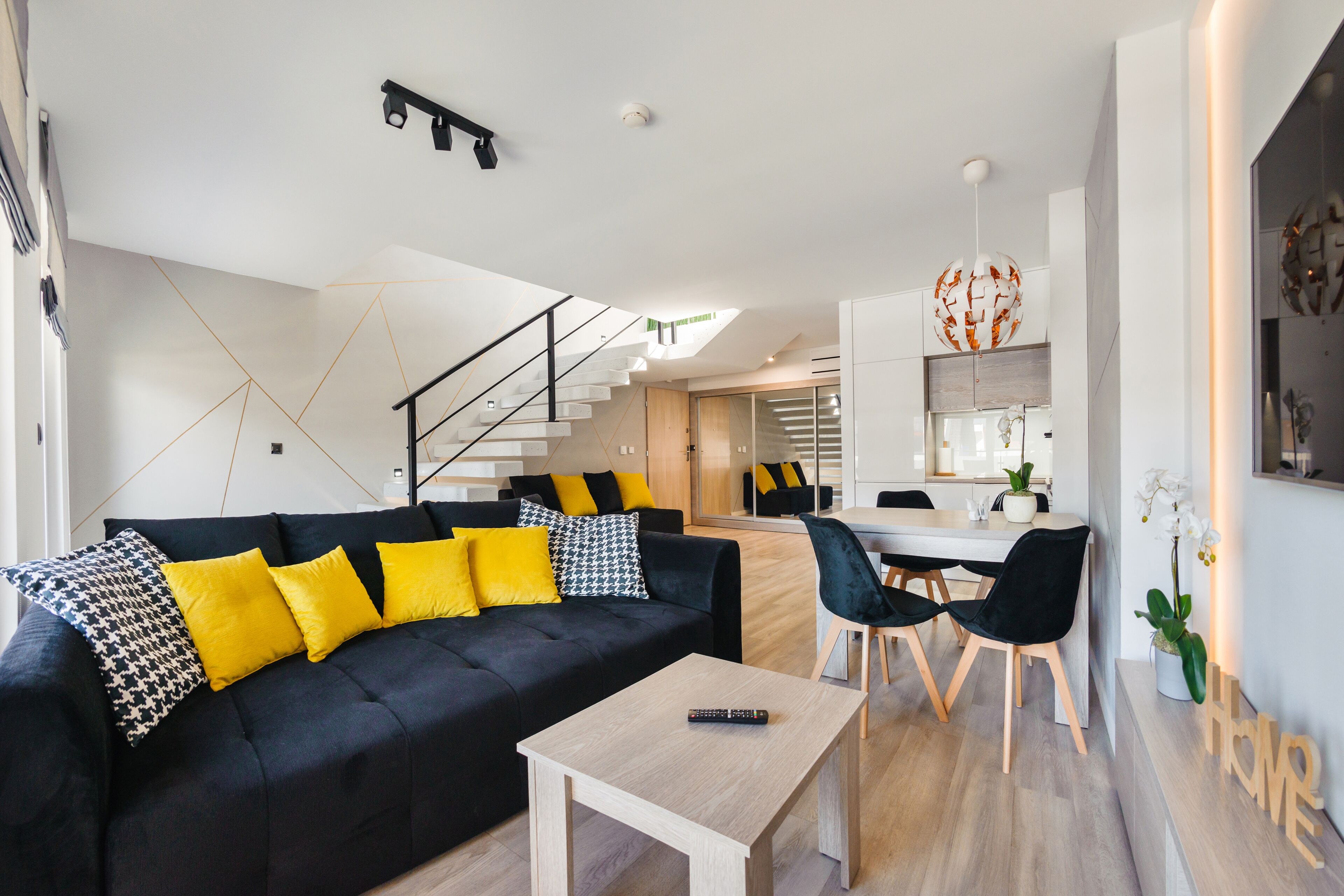 A modern living room with a black sofa, yellow cushions, a wooden coffee table, and a dining area with a white table and black chairs.