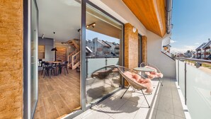 Un balcón moderno con piso de madera, un comedor con mesa y sillas, y una zona de estar con una silla y una mesa.
