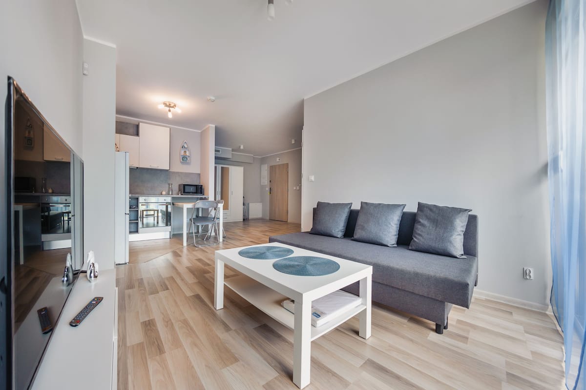 A modern living room with a grey sofa, a white coffee table, and a kitchen in the background.