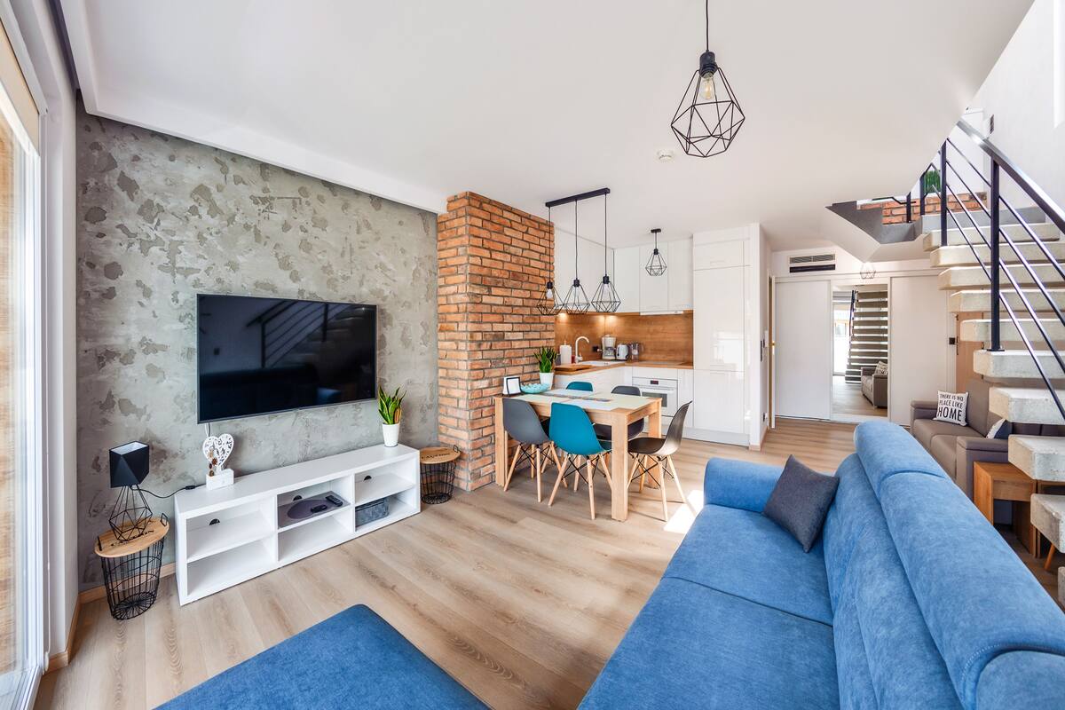 A modern living room with a TV, seating area, and a kitchen in the background.