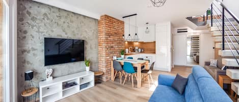 A modern living room with a TV, seating area, and a kitchen in the background.