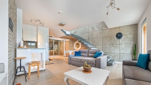 Un salón moderno con una mesita de centro blanca, un sofá gris y una escalera con un espejo circular.
