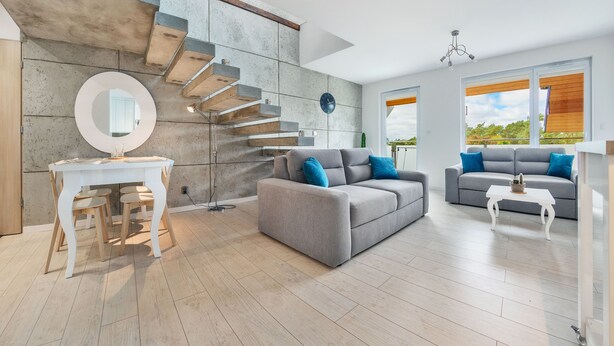 Una sala de estar moderna con una escalera, un espejo redondo, un sofá gris y una mesa de centro blanca.
