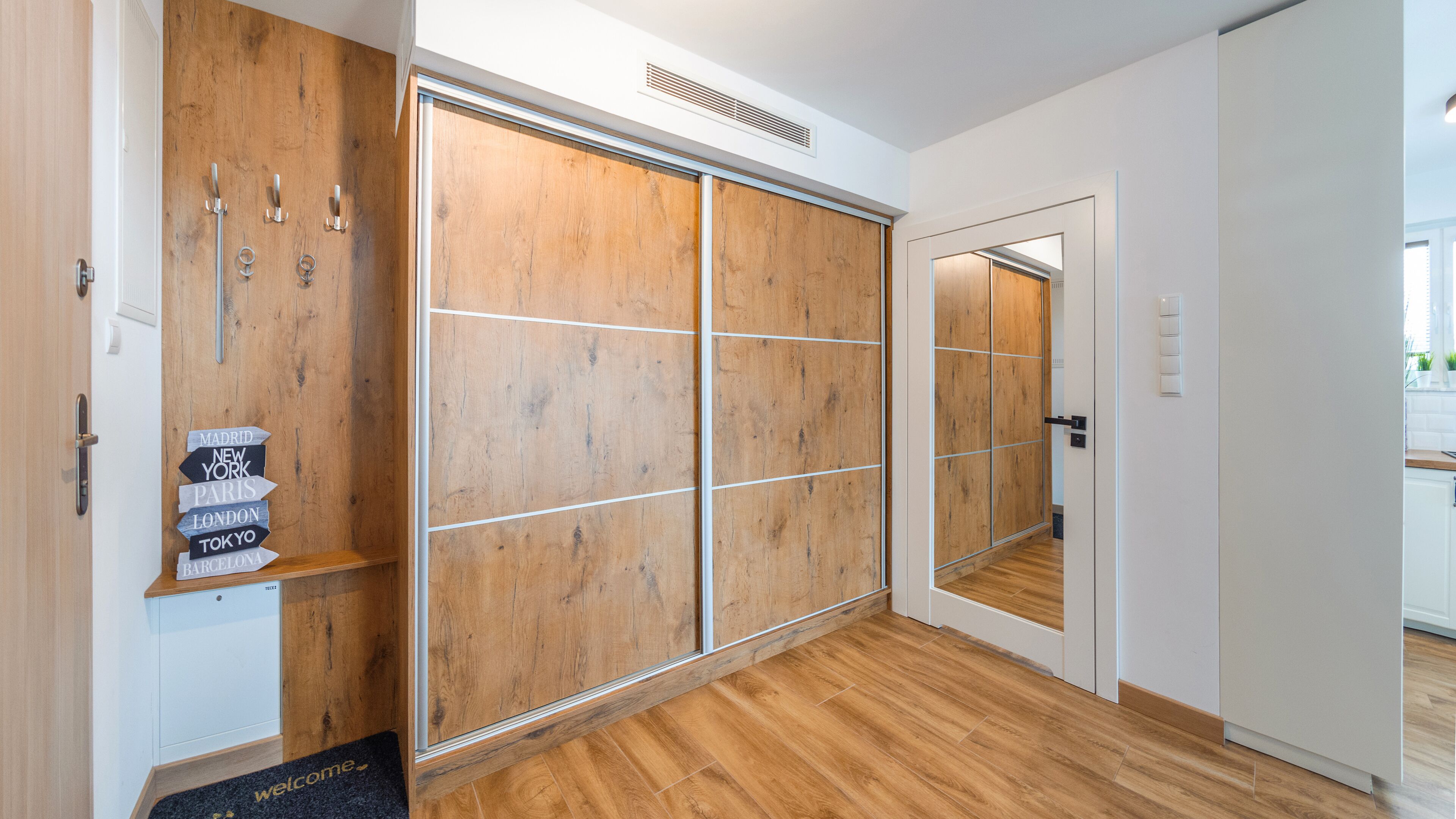 A modern hotel room with a wooden wardrobe, a mirror, and a welcome mat.