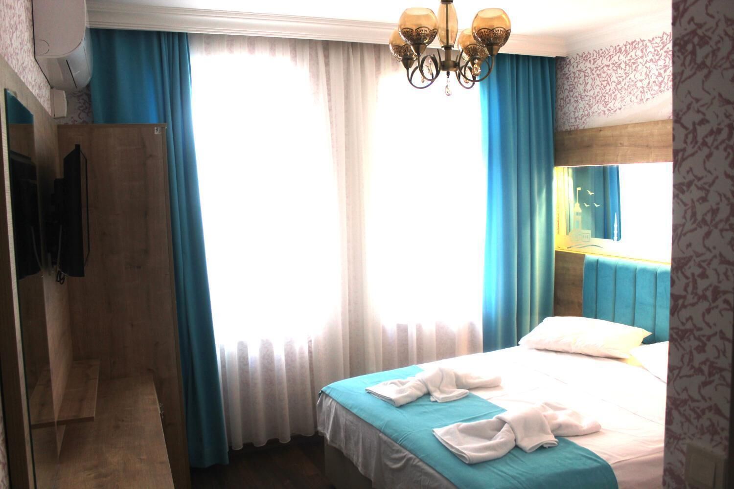 A hotel room with a bed, a shower area, a mounted TV, and a chandelier.