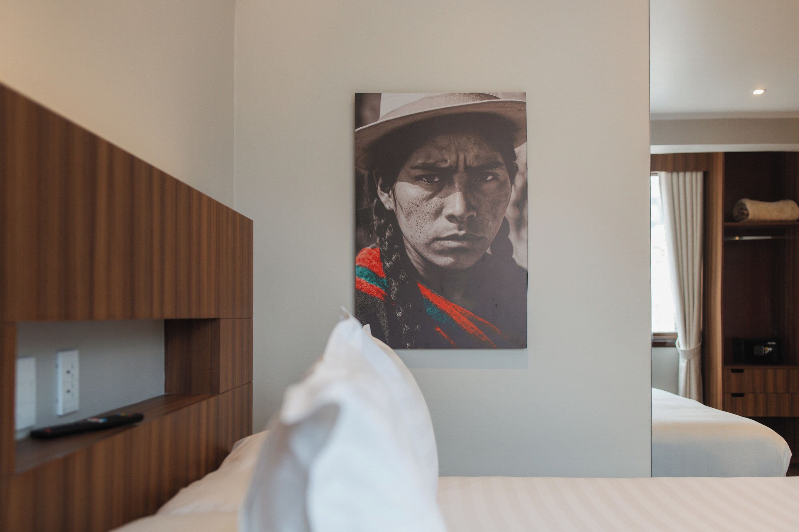 A hotel room with a bed, a wooden wardrobe, and a wall-mounted artwork.