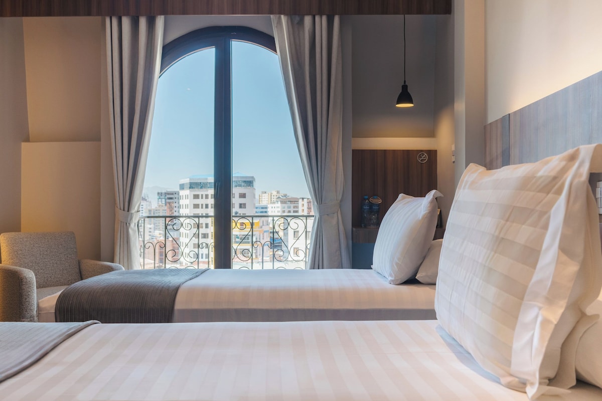 A hotel room with a large window, a bed, a chair, and a nightstand.