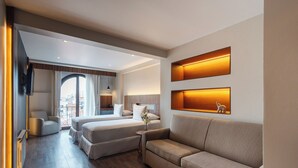 A modern hotel room with a large bed, a sofa, and a desk. There is a window with curtains, a flat-screen TV mounted on the wall, and a small table with a vase of flowers. - DREAM By Stannum Hotel (La Paz)