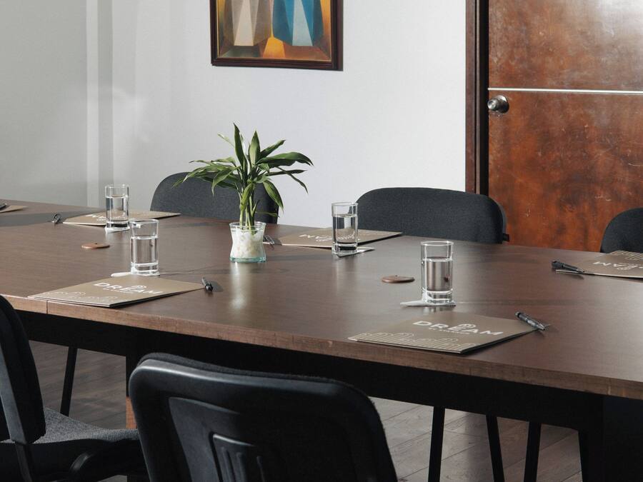 A conference room with a long table, chairs, a potted plant, and a framed artwork on the wall.