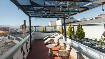 Una terraza en la azotea con mobiliario exterior, techo de vidrio y vistas a la ciudad.