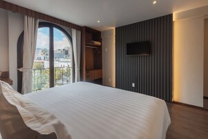 Habitación de hotel moderna con una cama grande, un televisor montado en la pared y vistas de la ciudad a través de un ventanal.