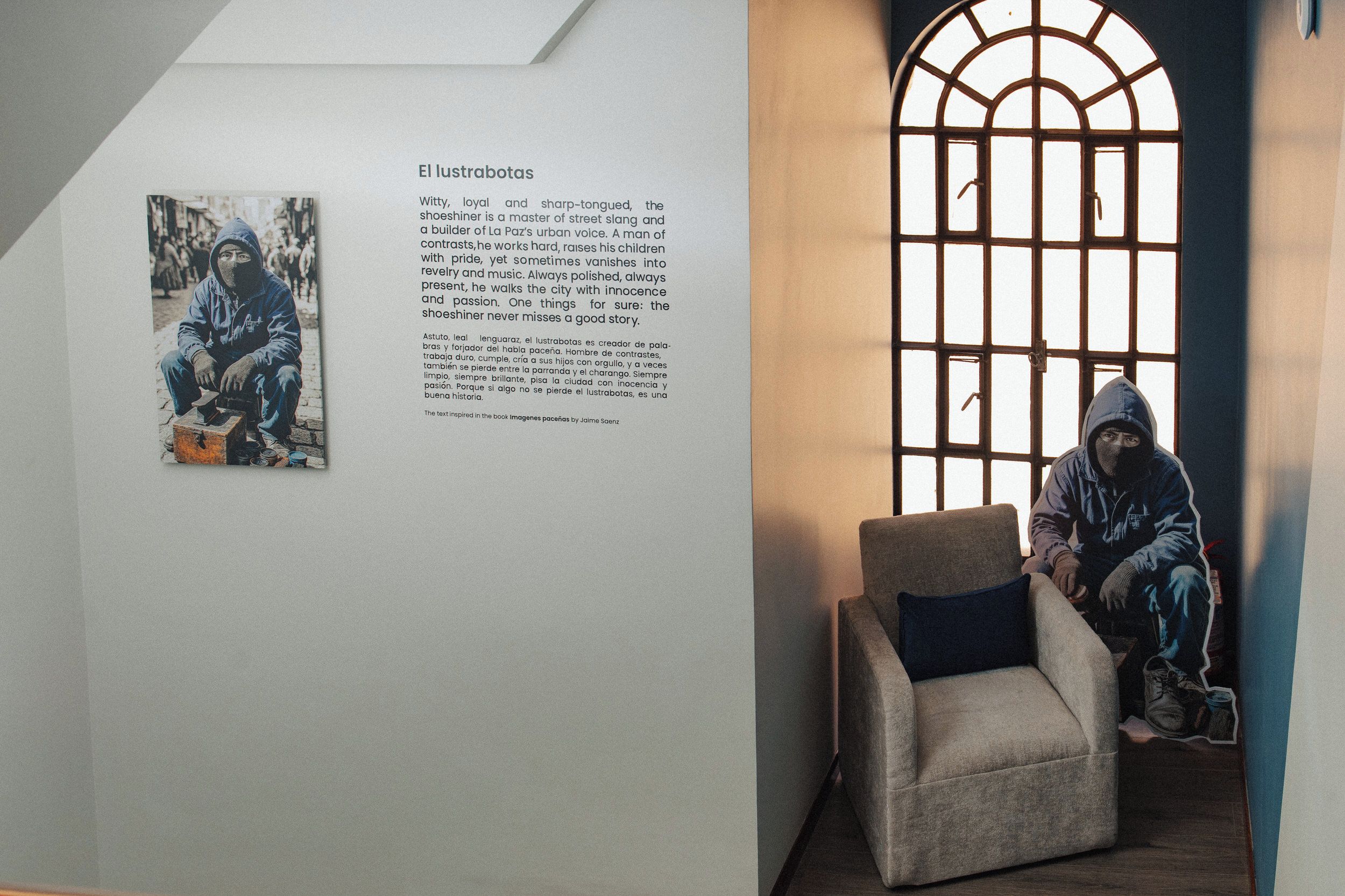 A room with a large window, a chair, and a wall-mounted text panel describing a shoe shiner.