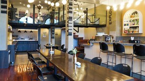 A modern bar area with a long counter, multiple seating options, and a visible kitchen area. - DREAM By Stannum Hotel (La Paz)