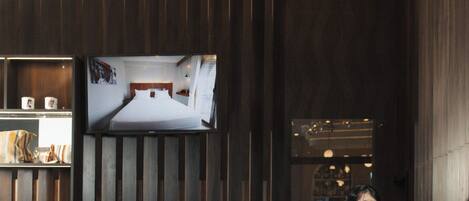 A hotel reception desk with a modern design, including a dark wood panel wall, a flat-screen TV, and a unique spherical light fixture.