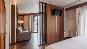 A hotel room with a bed, a sofa, a TV mounted on the wall, and a view of the outdoors through a large window. - DREAM By Stannum Hotel (La Paz)