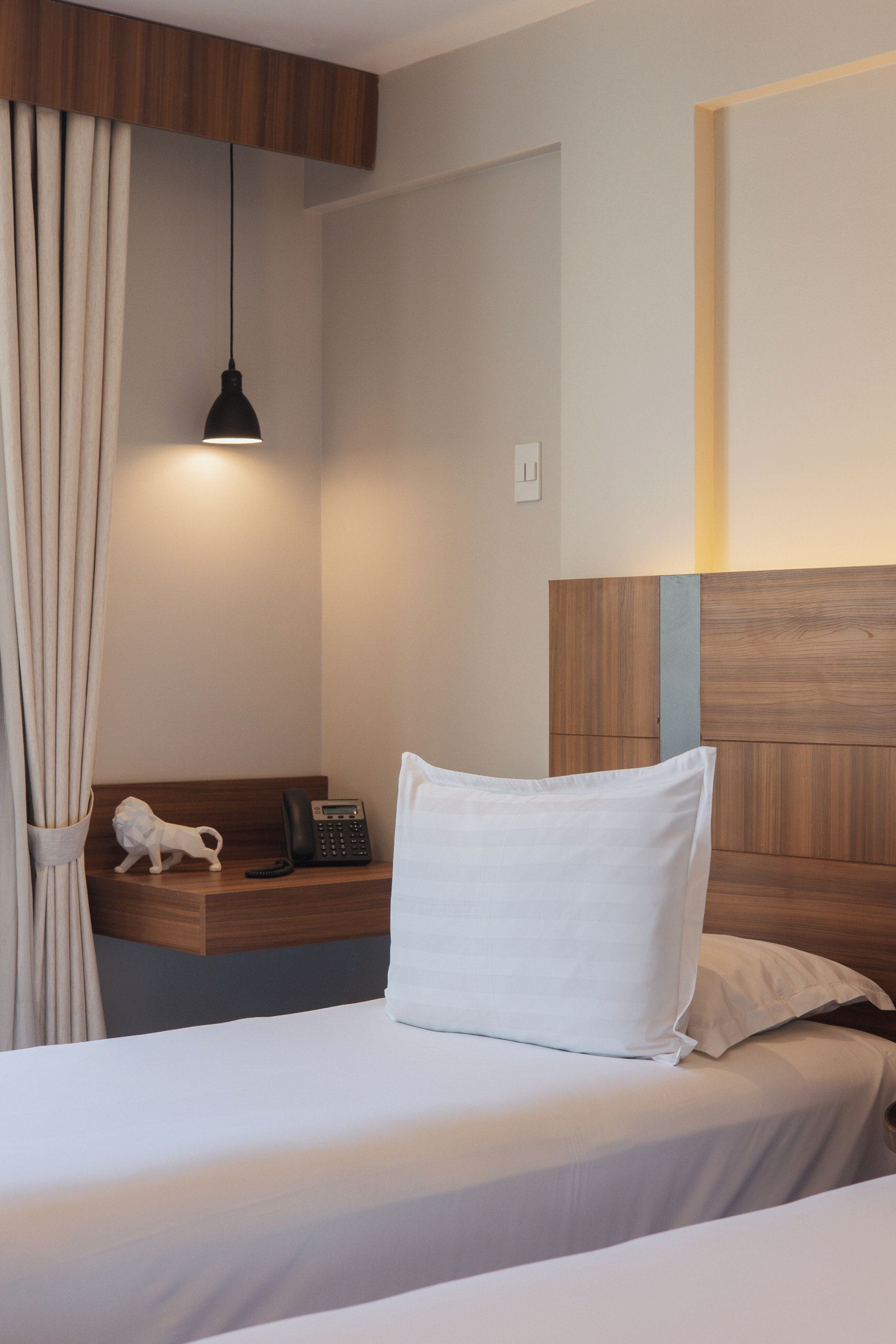 Una habitación de hotel con una cama, una mesita de noche con un teléfono, una lámpara y una cortina.
