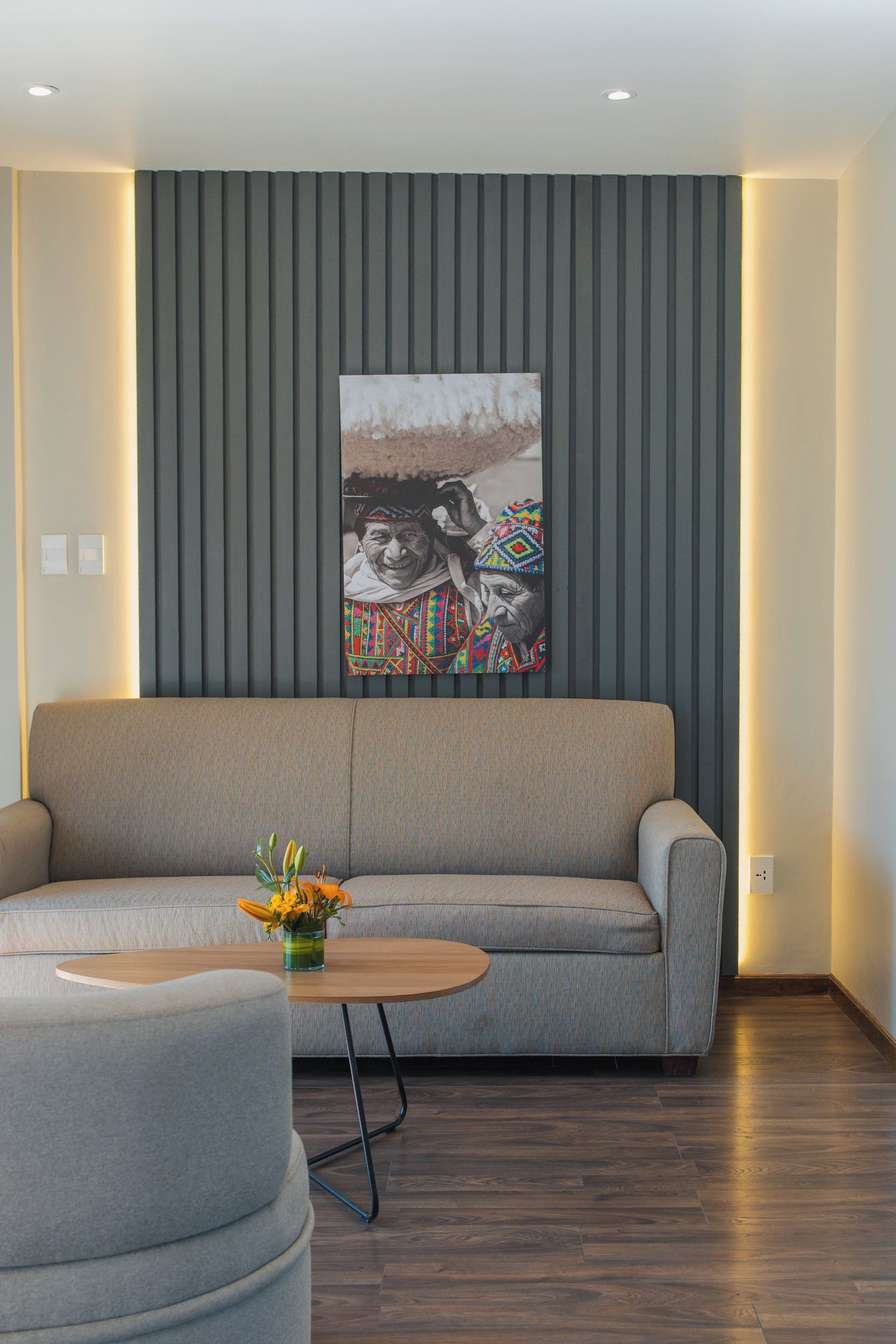 A modern living room with a grey sofa, a round coffee table with a vase of flowers, and a wall-mounted artwork.