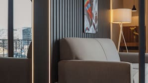 A modern hotel room with a sofa, a large window with a view of the city, a decorative wall panel, and a floor lamp. - DREAM By Stannum Hotel (La Paz)