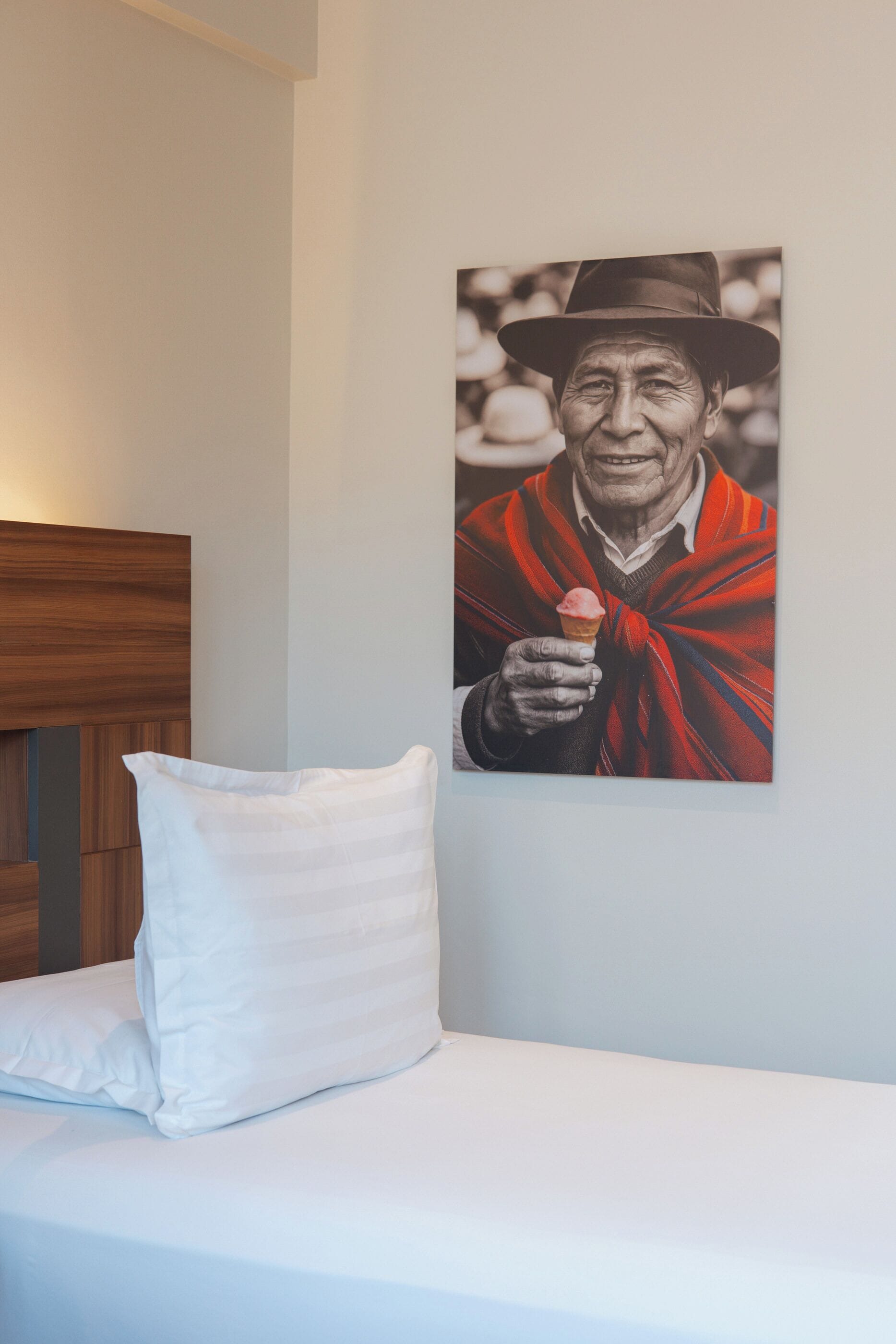Un dormitorio con una cama, un almohadón blanco y una obra de arte colgada en la pared que muestra a una persona sosteniendo un helado.