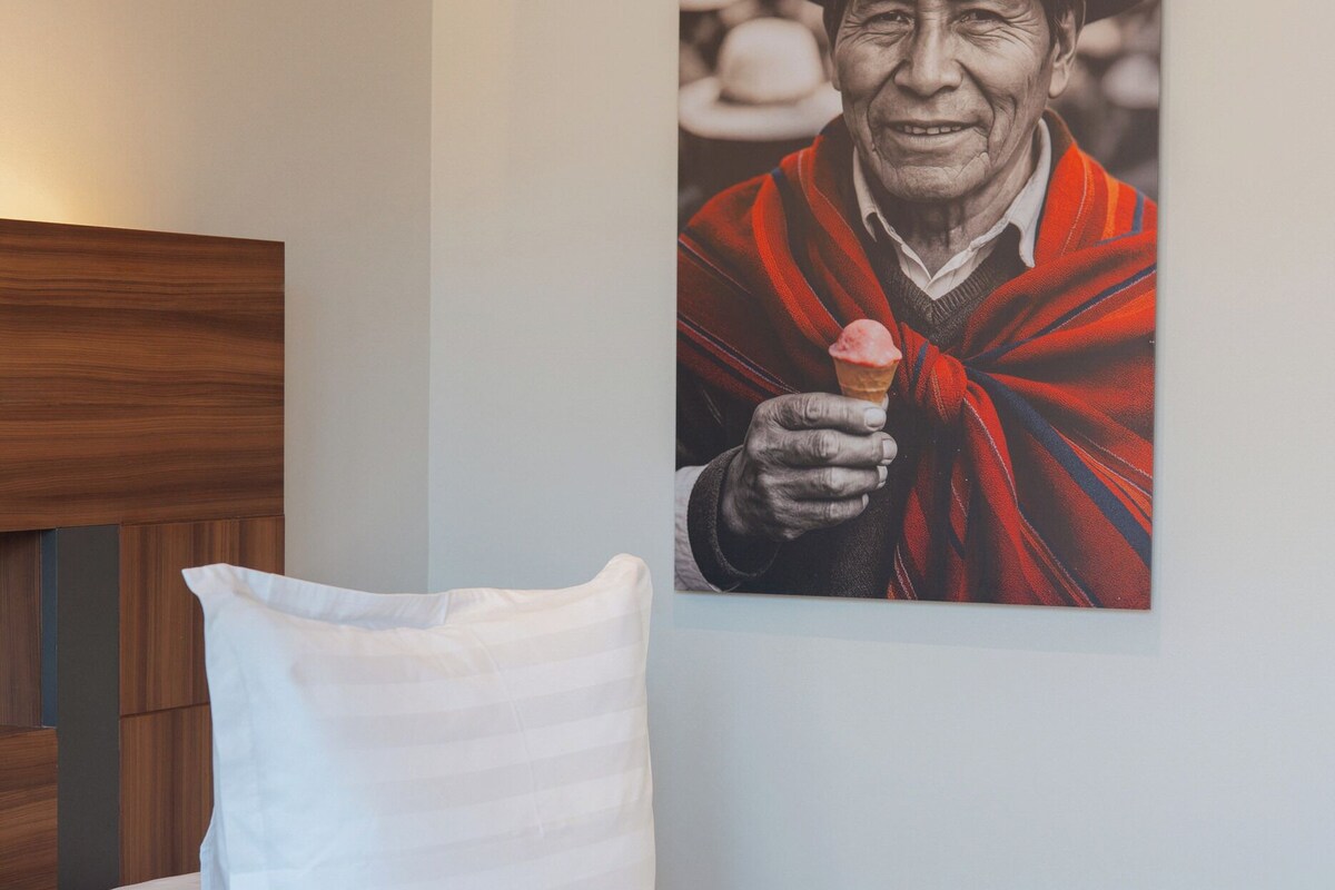 A bedroom with a bed, a white pillow, and a wall-mounted artwork of a person holding an ice cream cone.