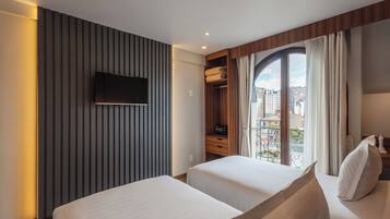 Hotelkamer met twee bedden, een aan de muur bevestigde televisie, een houten garderobe en een balkon met uitzicht op de stad.