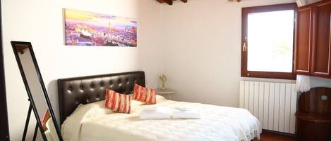 A bedroom with a bed, a painting on the wall, a window, and a radiator.