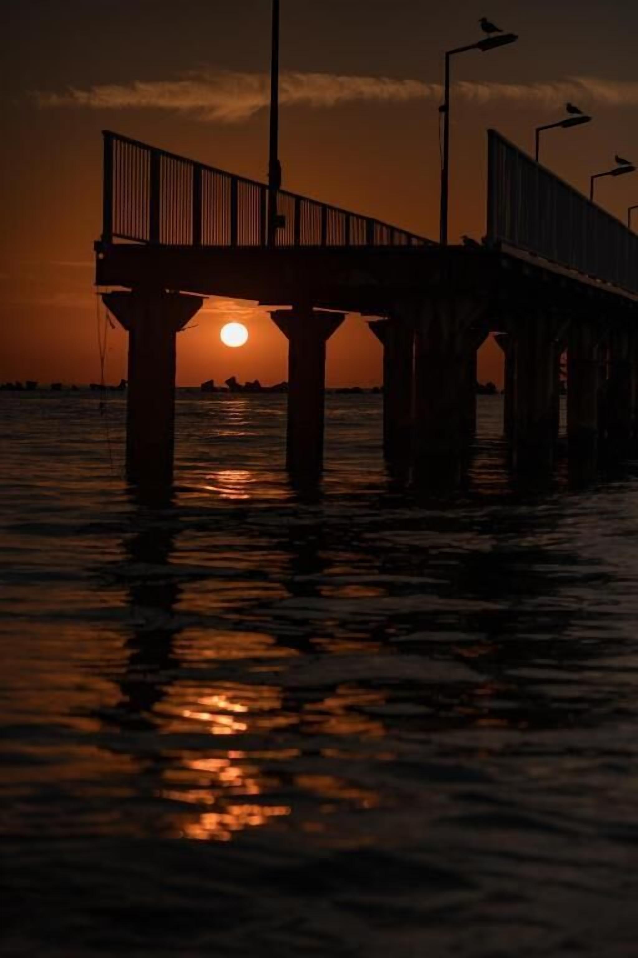 A pier extending over water with a sunset in the background.