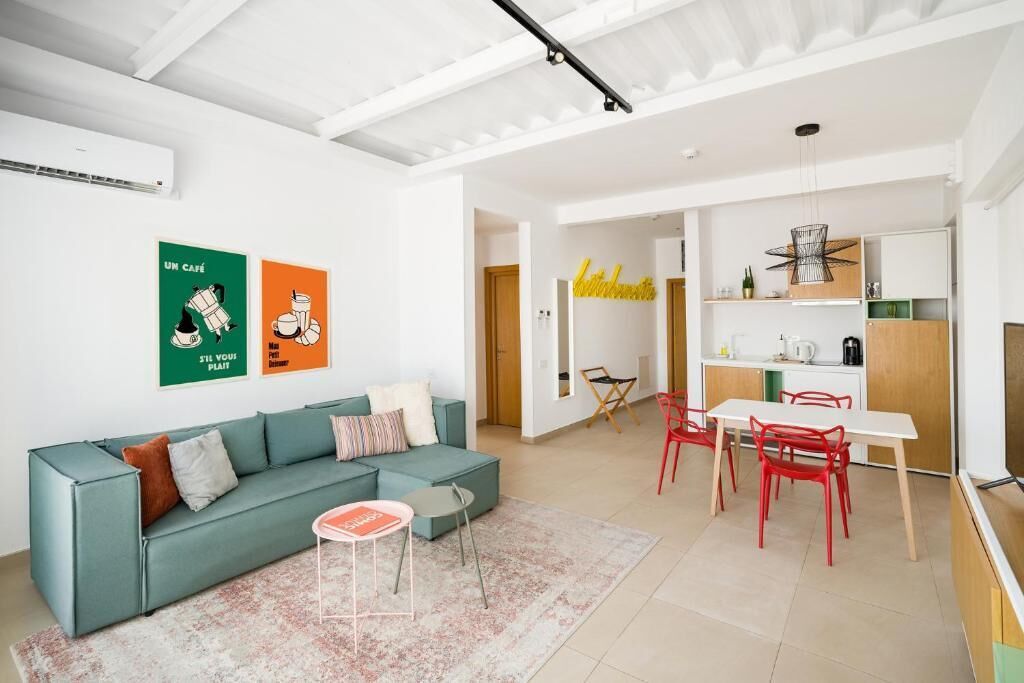 Un salon moderne avec un canapé de couleur turquoise, une petite table ronde et un coin repas comprenant des chaises rouges et une table blanche.