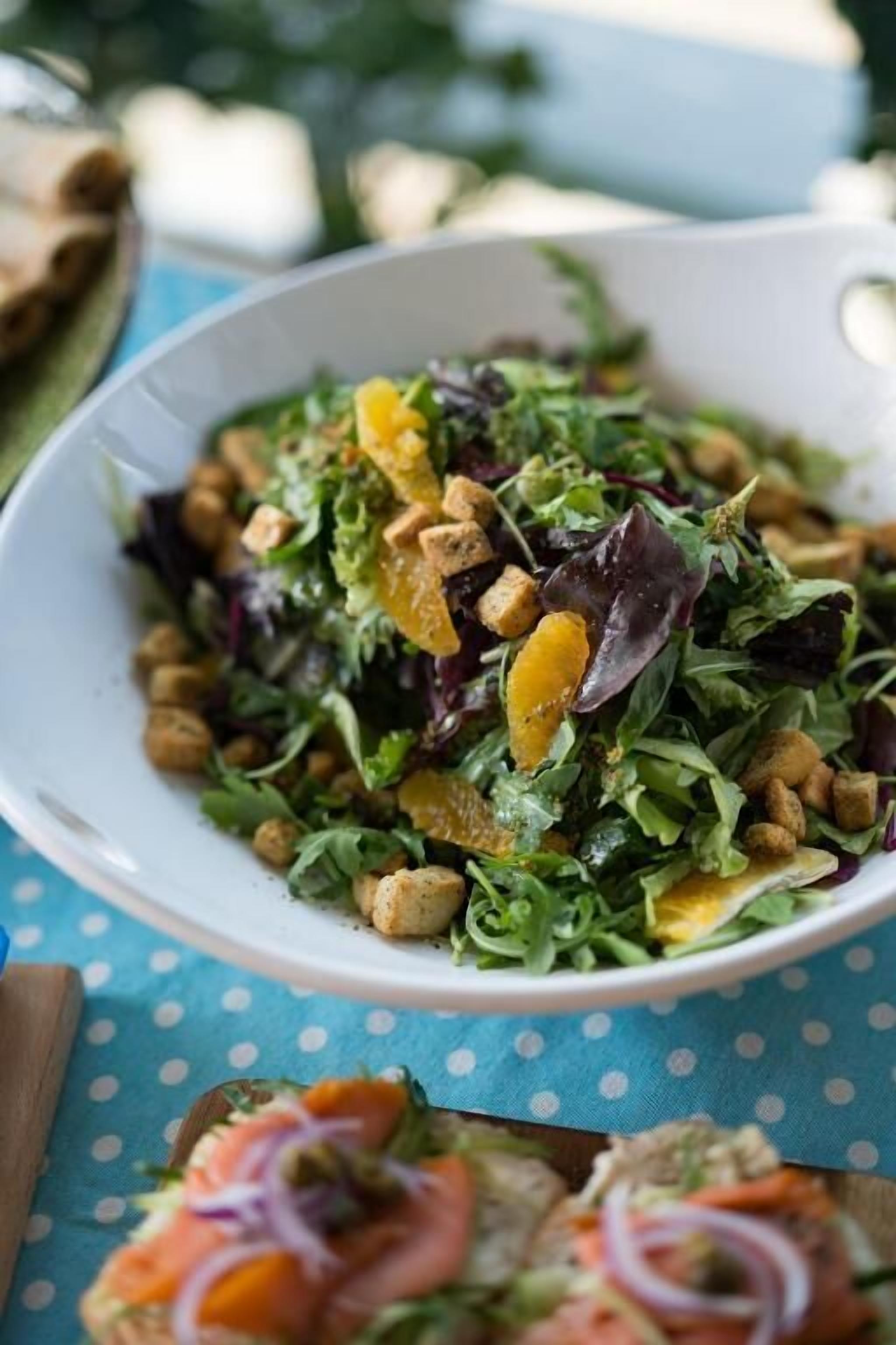A bowl of salad with various greens, chickpeas, and orange slices on a blue polka dot tablecloth.